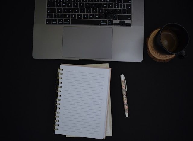 Macbook, café y libreta en un escritorio.